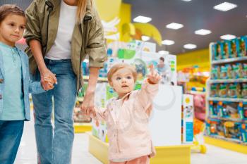 Mother with her little children in kids store. Mom with daughter and son together choosing toys in supermarket, family shopping