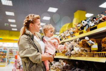 Mother with her little girl choosing toys in kids store. Mom and child in supermarket together, family shopping