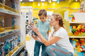 Happy mother with her little son choosing toys in kids store. Mom and child have a purchase in supermarket together, family shopping
