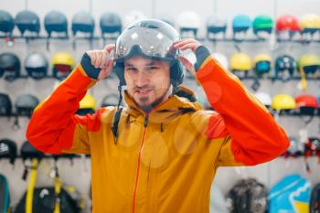 Man at the showcase trying on helmet for ski or snowboarding, side view, sports shop. Winter season extreme lifestyle, active leisure store, buyers choosing protect equipment