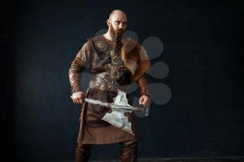 Viking with axe dressed in traditional nordic clothes. Ancient warrior, studio with black walls