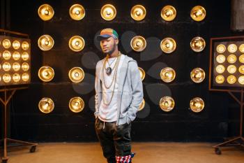 Black rapper in cap on stage with spotlights on background. Rap performer on scene with lights, underground music, urban style