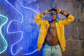 Black rapper in underpass neon light on background. Rap performer in club with grunge walls, underground music