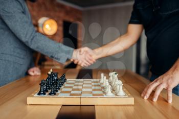 Male chess players shake hands before the game. Two chessplayers begin the intellectual tournament indoors. Chessboard on wooden table