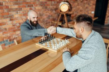 Chess players shake hands before the game. Two male chessplayers begin the intellectual battle indoors.