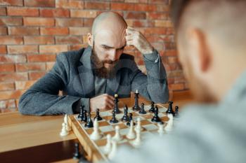 Male chess players playing, thinking process. Two chessplayers begin the intellectual tournament indoors. Chessboard on wooden table, strategy game