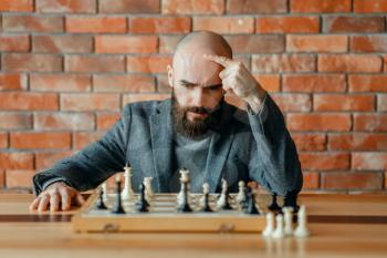 Male chess player understood that he lost, checkmate. Chessplayer at board, front view, intellectual tournament indoors. Chessboard on wooden table, strategy game