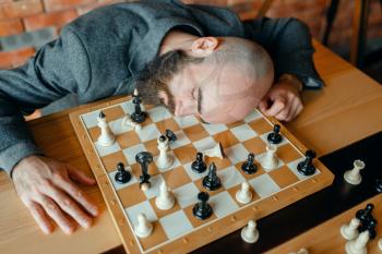 Tired male chess player sleeping on the board. Chessplayer playing, intellectual tournament indoors. Chessboard on wooden table, strategy game