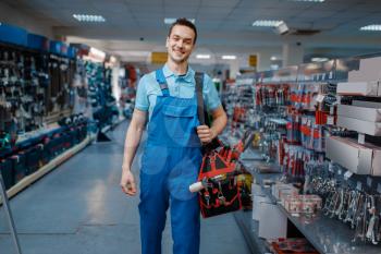 Male worker in uniform holds toolbox in tool store. Choice of professional equipment in hardware shop