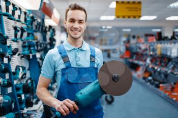 Male worker in uniform holds angle grinder in tool store. Choice of professional equipment in hardware shop, instrument supermarket