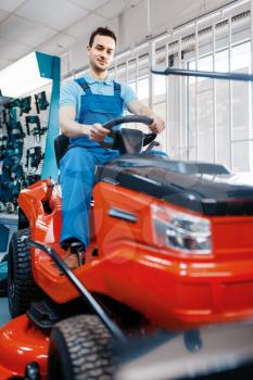 Male worker sitting on lawn mower in tool store. Choice of professional equipment in hardware shop, electrical and gas instrument supermarket