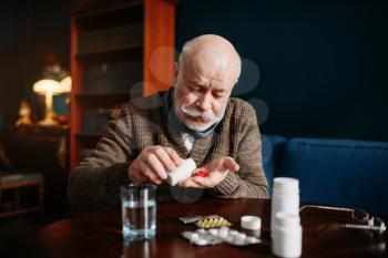 Elderly man hand with pills, home office on background, age-related diseases. Mature senior is ill and being treated in his house