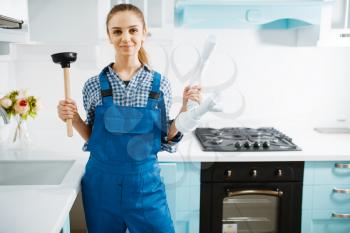 Cute female plumber in uniform holds plunger and pipe, clog in the kitchen. Handywoman repair sink, sanitary equipment service at home