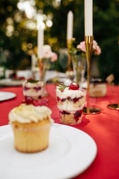 Table setting, tea party with fresh cake, nobody. Luxury silverware on red tablecloth, tableware outdoors. Wedding celebration on summer meadow