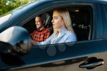 Female student and male instructor in car, driving school. Man teaching a woman to drive vehicle. Driver's license education