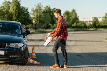 Female student knocks down traffic cone, lesson in driving school. Man teaching lady to drive vehicle. Driver's license education