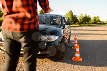 Female student passes between cones, lesson in driving school. Man teaching lady to drive vehicle. Driver's license education