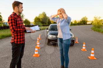 Stressed female student and instructor with checklist on road, lesson in driving school. Man teaching lady to drive vehicle. Driver's license education