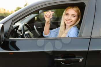 Happy woman with keys poses in car, lesson in driving school. Lady learns to drive vehicle. Driver's license education