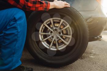 Male worker in uniform fixing problem with tire, tyre service. Vehicle repair service or business, man repairing broken wheel