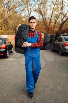 Male worker in uniform holds new tyre, tire service. Vehicle repair service or business, man change wheels on automobile