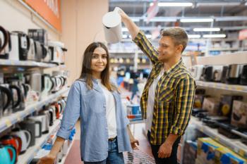 Young couple jokes with electric kettles in electronics store. Man and woman buying home electrical appliances in market