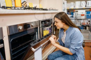 Young woman choosing electric oven in electronics store. Female person buying home electrical appliances in market, housewife looking goods in shop