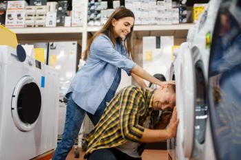 Family couple jokes with washing machine in electronics store. Man and woman buying home electrical appliances in market