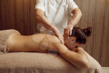 Male masseur hands pampering neck to young woman in towel, professional massage. Massaging and relaxation, body and skin care. Attractive lady in spa salon