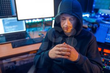 Hacker in mask and hood sitting at his workplace with laptops and PC, information hacking. Internet spy, illegal lifestyle