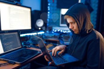 Hacker in hood shows thumbs up at his workplace with laptop and PC, password or account hacking. Internet spy, crime lifestyle