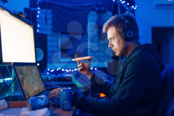 Male gamer drinking an energy drink at his workplace with laptop and desktop PC, gaming night lifestyle. Computer games player in his room with neon light, streamer