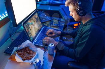 Male gamer in headphones playing on laptop and desktop PC, gaming lifestyle, night tournament. Computer games player in his room with neon light, streamer
