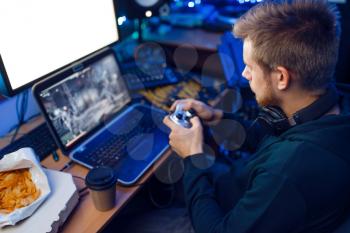 Male gamer in headphones holds joystick and playing videogame on console or desktop PC, gaming lifestyle, cybersport. Computer games player in his room with neon light, streamer