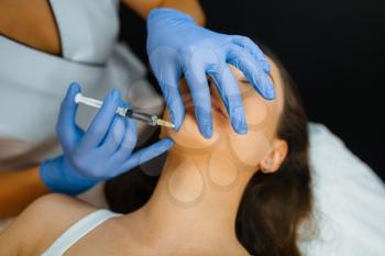 Cosmetician in gloves gives chin botox injection to female patient on treatment table. Rejuvenation procedure in beautician salon. Doctor with syringe and woman, cosmetic surgery against wrinkles