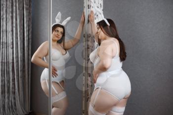 Overweight woman poses at the mirror in erotic bunny costume. Sexy overweight girl with big breast, perverse large size lady