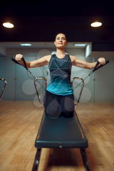 Slim woman in sportswear, pilates training on exercise machine in gym, front view. Fitness workuot in sport club. Athletic female person, aerobics indoor, body stretching