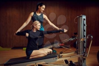 Slim woman in sportswear on pilates training with instructor on exercise machine in gym. Fitness workuot in sport club. Athletic female person, aerobics indoor, body stretching