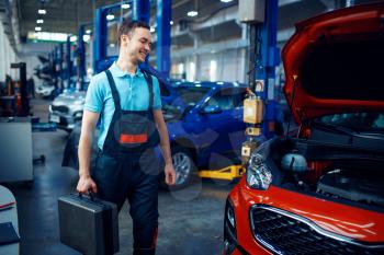 Worker in uniform holds a toolbox, car service station. Automobile checking and inspection, professional diagnostics and repair