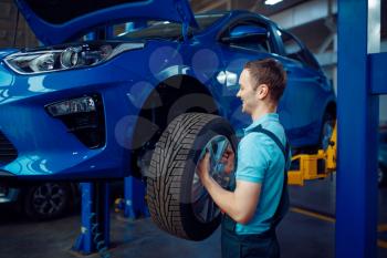 Worker in uniform removes wheel from vehicle, car tire service station. Automobile checking and inspection, professional diagnostics and repair