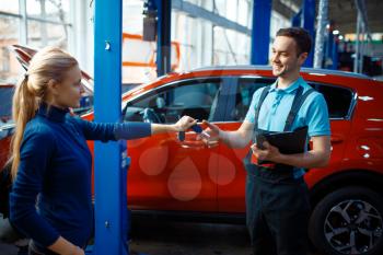 Female driver gives keys to worker in uniform, car service station. Automobile checking and inspection, professional diagnostics and repair