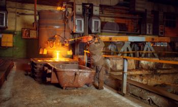 Steelmaker in helmet pours liquid metal from basket, steel factory, metallurgical or metalworking industry, industrial manufacturing of iron production on mill
