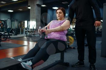 Overweight woman with trainer doing exercise in sport club, fitness training with instructor. Female person struggles with excess weight, aerobic workout against obesity, gym
