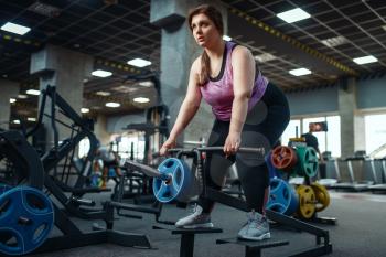 Overweight woman doing exercise with bar in gym, active training. Obese female person struggles with excess weight, aerobic workout against obesity, sport club