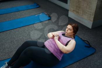 Overweight woman doing exercise on mat in gym, active training. Obese female person struggles with excess weight, aerobic workout against obesity, sport club