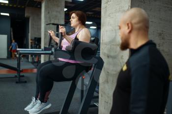 Tired overweight girl with trainer in sport club, fitness training with instructor. Female person struggles with excess weight, aerobic workout against obesity, gym