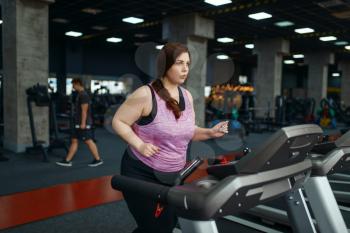 Overweight woman doing exercise on treadmill in gym, active training. Obese female person struggles with excess weight, aerobic workout against obesity, sport club
