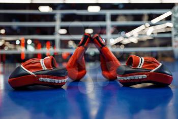 Pair of red boxing gloves and pads on ring, nobody. Box or kickboxing sport concept, equipment for training, fighting martial arts