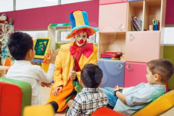 Funny clown play with cheerful children together. Birthday party celebrating in playroom, baby holiday in playground. Childhood happiness