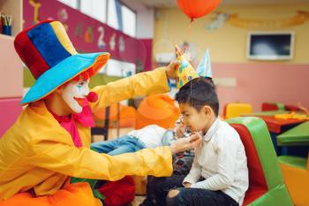 Funny clown puts a cap on the little boy's head. Birthday party celebrating in playroom, baby holiday in playground. Childhood happiness, childish leisure